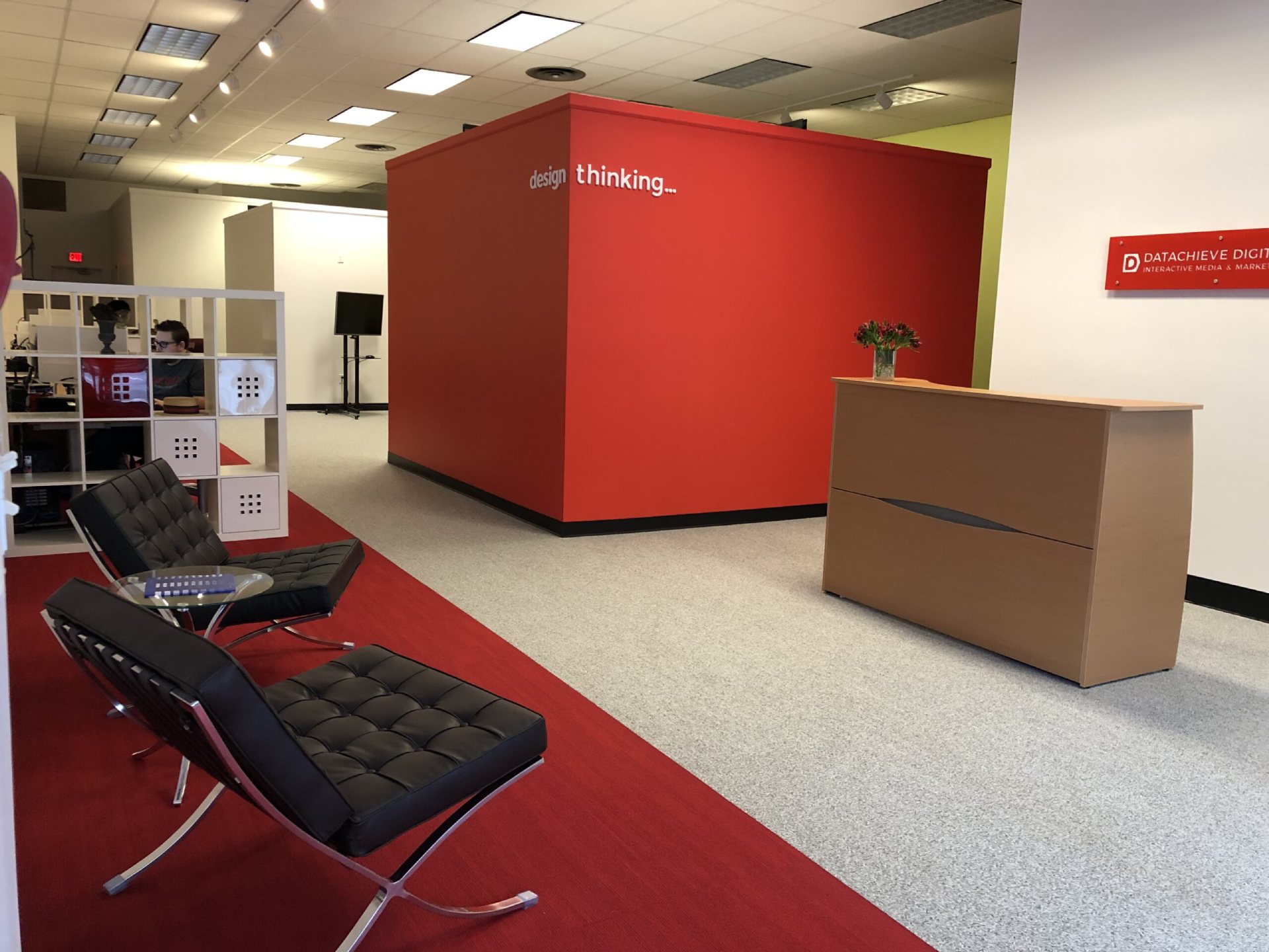 Modern office lobby with black leather chairs, a wooden reception desk, and a bold red accent wall that reads 