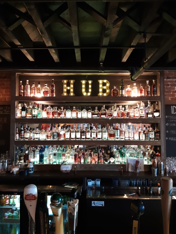 A bar shelf filled with various bottles of alcohol, illuminated by warm lights. The word 