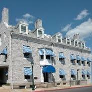 A large stone building with multiple dormer windows and blue-and-white striped awnings over its windows and entrance, set against a clear blue sky.