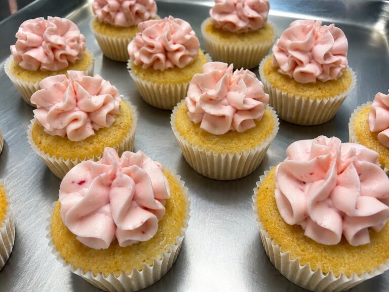 Several yellow cupcakes with light pink icing on top sitting on a metal tray.