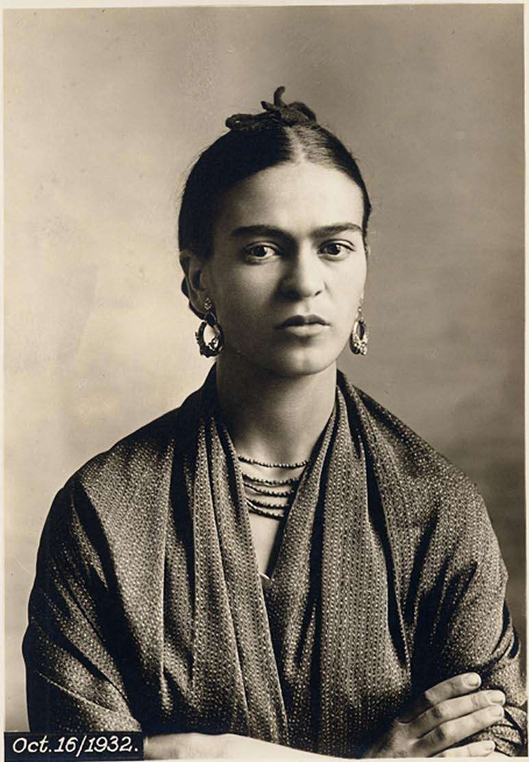 A black-and-white portrait of Fundraiser-Frida with dark hair tied back, wearing earrings, a necklace, and a textured shawl. She faces the camera with a serious expression. The date "Oct. 16/1932" appears in the lower left corner.