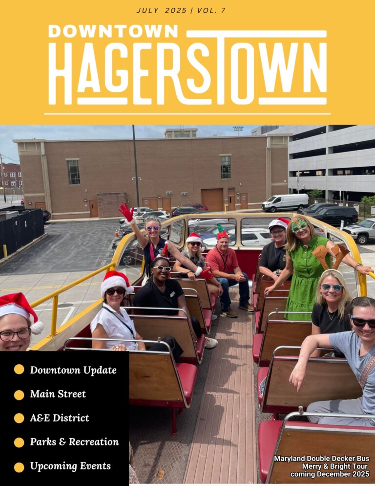 A group of people, some in festive holiday attire, sit and smile on the top deck of a yellow double-decker bus in a city parking lot. A list of magazine contents appears on the left.