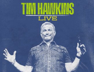 A man stands on stage holding a microphone, smiling with arms open wide. The text above him reads "TIM HAWKINS LIVE" in bold yellow and white letters on a blue background.