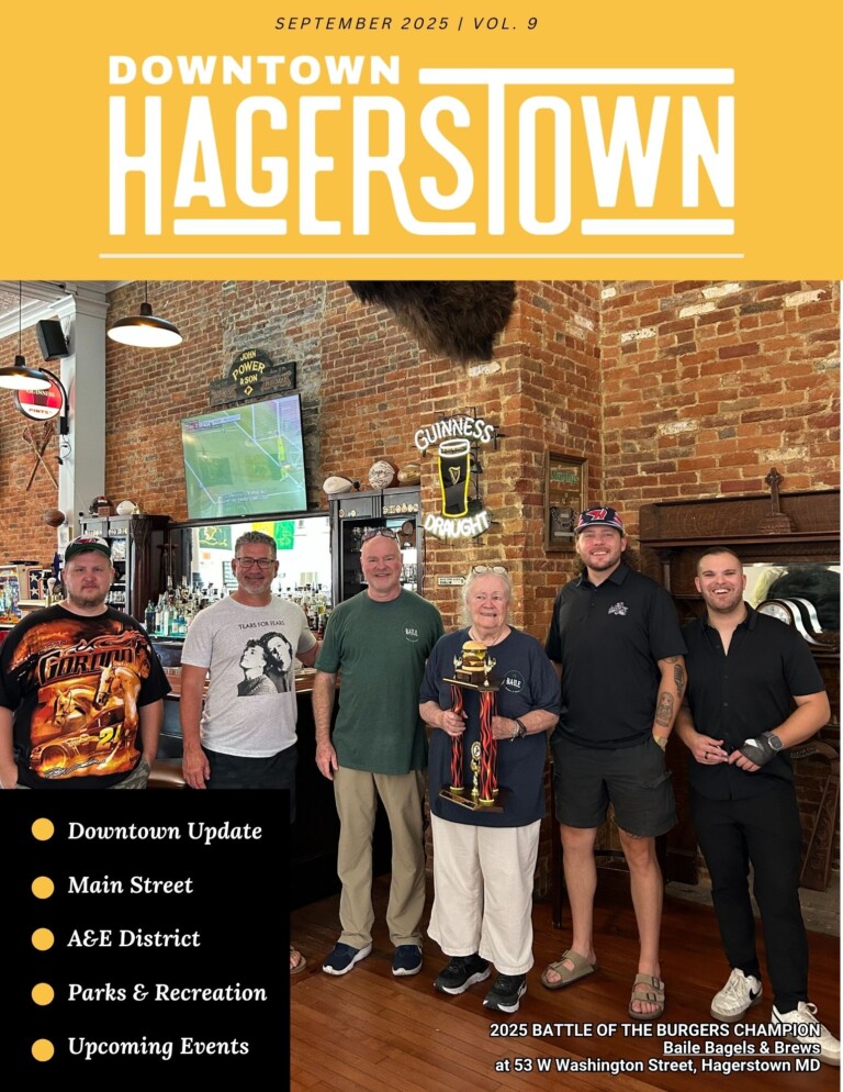 Five people stand inside a restaurant holding a trophy, posing for a group photo. The brick walls and bar decor add charm. Text lists magazine features, newsletter highlights, and a caption notes a burger competition winner.