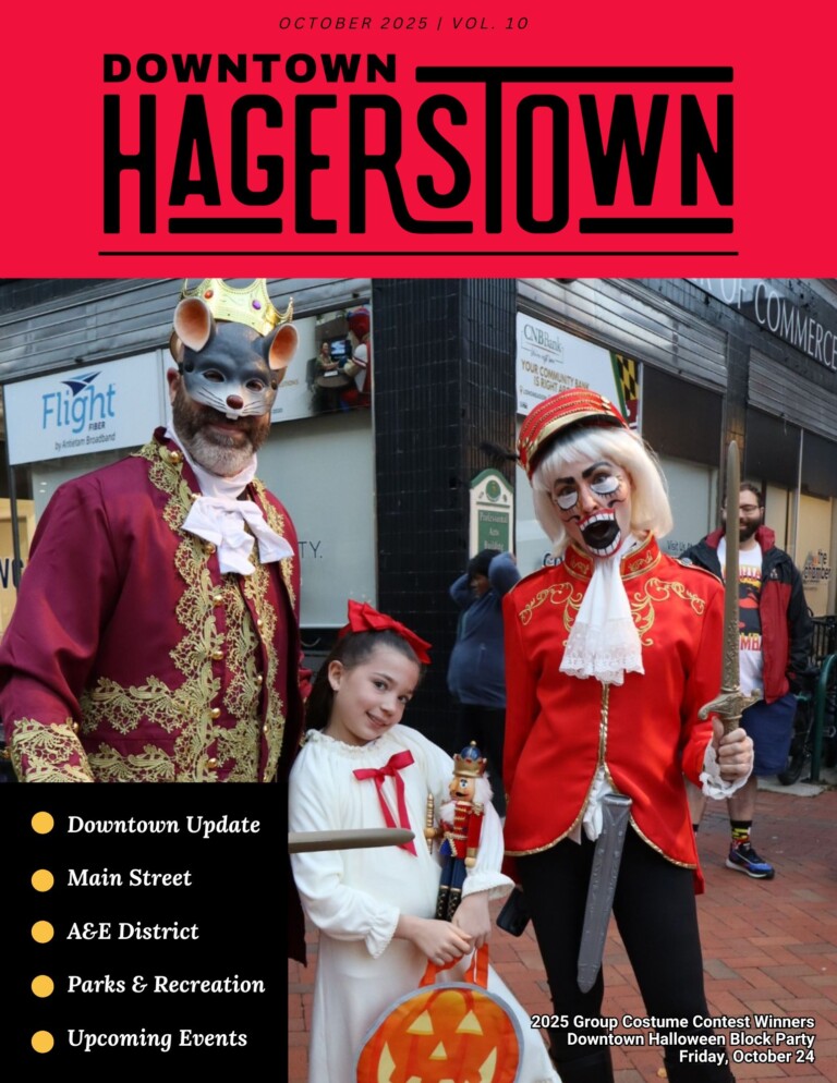 Three people in Halloween costumes pose together on a city street for a newsletter photo: an adult as a mouse king, a child in a white dress with a pumpkin bucket, and an adult ringmaster with a painted face.