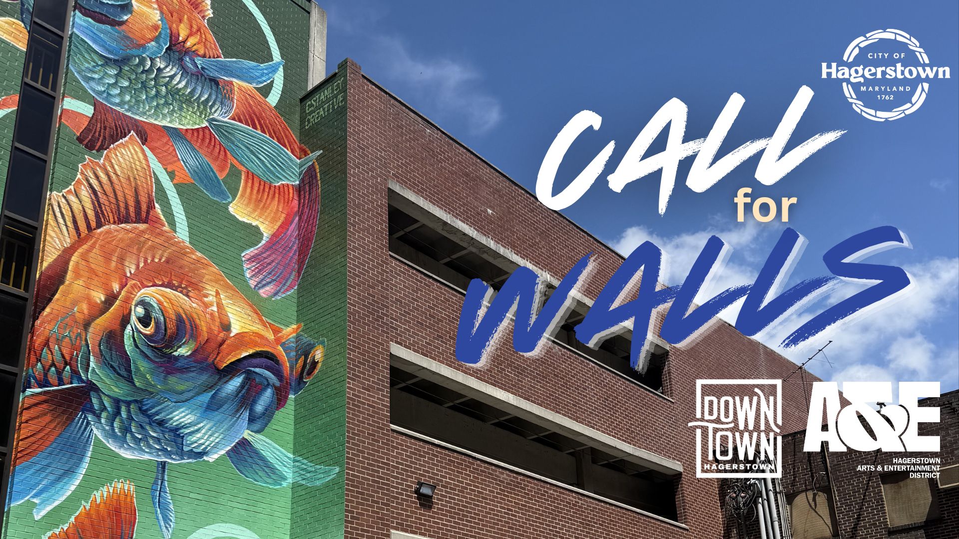 A vibrant mural of colorful fish decorates a building wall next to a brick structure. The text 