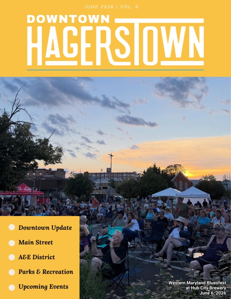 A large crowd sits on lawn chairs at an outdoor event during sunset, with tents, trees, and buildings in the background. The magazine cover reads “Downtown Hagerstown” and highlights newsletter updates and features.
