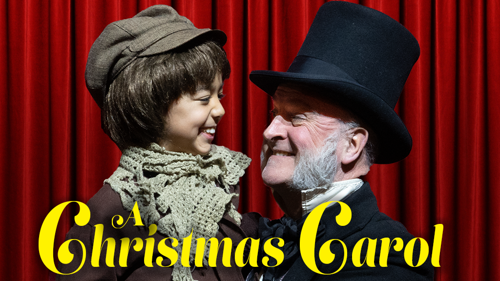 A child in old-fashioned clothes smiles at an older man in a top hat and scarf. They stand in front of red stage curtains. The text “A Christmas Carol” is in large yellow letters at the bottom.
