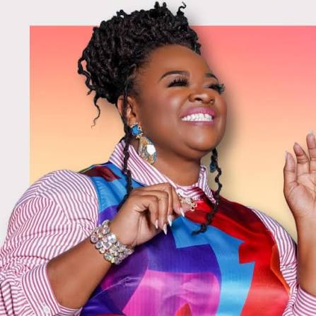 Smiling woman with braided hair wearing a colorful dress, striped shirt, large earrings, and bracelets, standing in front of a pink and yellow gradient background.