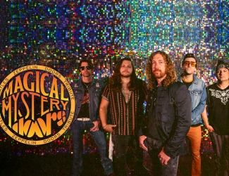 Five men stand in front of a sparkling, colorful backdrop. On the left, a round sign reads “MAGICAL MYSTERY.” They wear casual, rock-inspired clothing and sunglasses, suggesting they are a band.