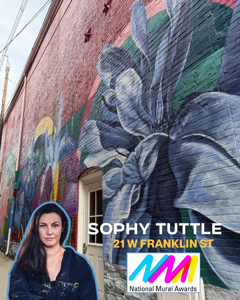 A large, vibrant mural featuring intricate florals is painted on a brick building. A woman stands in front, with text: “Sophy Tuttle, 21 W Franklin St.” The National Mural Awards logo appears at the bottom.