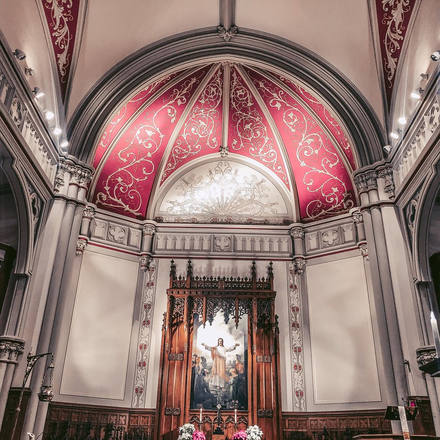 Interior of a church sanctuary, a house of worship featuring an ornate wooden altar framed by a large painting of Jesus and a domed ceiling with red decorative paneling.