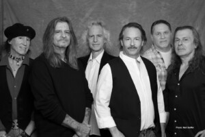 Black and white studio portrait of six men standing in a row against a textured backdrop.